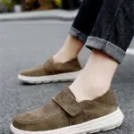 A person wearing rolled-up jeans and New Retro Men Shoes Light Shock Absorbing Flat Sneakers Wholesale Customized Leather Loafers with white soles stands on a paved surface.