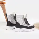 A pair of New Arrivals waterproof, fur-lined women’s snow boots with a PU upper, anti-slip thick white soles, black accents, and adjustable lock lace-up zipper design displayed on a white background.