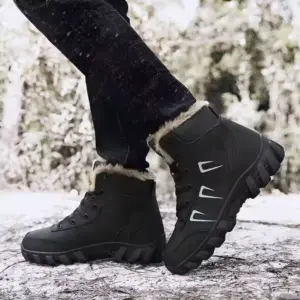 A person wearing Customized Plush Laced Winter Snow Boots Anti Slippery Warm Waterproof Rubber PU Cotton Shoes and dark pants stands outdoors on a snowy, wooded path.