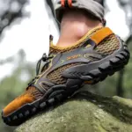Close-up of a person wearing OEM ODM Wholesale Customized Outdoor Hollow Mesh Hiking Shoes Anti-slip Flats EVA Rubber Water Shoes, standing on a mossy rock outdoors.