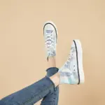 A person wearing Hot Sale Zapatos Women Casual Custom Canvas Sneaker Shoes with a blue print and blue jeans poses with feet crossed against a beige background.