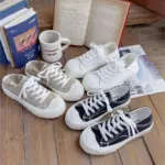 Three pairs of Breathable Designed Women Shoes Solid Cotton Sneakers Slip on Low Top Women Canvas Shoes in beige, white, and black are displayed on a wooden floor beside books, magazines, and a coffee mug, offering stylish and versatile everyday options.