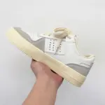 A hand holds the Factory Wholesale Retro Breathable Men Sneakers—vintage-style white and beige shoes with grey accents—against a plain white background.
