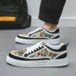 A person stands on a gray floor wearing Wholesale Factory 2024 Rubber Embossing Canvas Shoes, featuring laced, multicolored tapestry-style design with black trim and white laces.