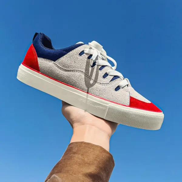 A hand holds up a Customizable Retro Mixed Stylish Plush Walking Sneaker for women, featuring gray with red and navy accents and white laces, against a clear blue sky.