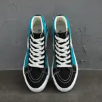 A pair of 2024 Fashion Breathable Mesh Casual Wholesale Sports Running Sneaker Fitness Walking Style Shoes for Men New Style in black, white, and teal with white laces is displayed side by side on a gray textured floor against a gray wall.