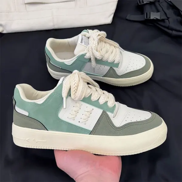 A hand holds a Factory Wholesale Retro Breathable Men Sneaker in green and white with cream laces; another matching sneaker is on a black surface in the background.