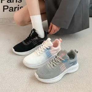 A person in a grey outfit and white socks is putting on a black Factory Custom Spring New Styles Sports Sneaker. Two more sneakers, one white and one grey, are on a beige carpet.