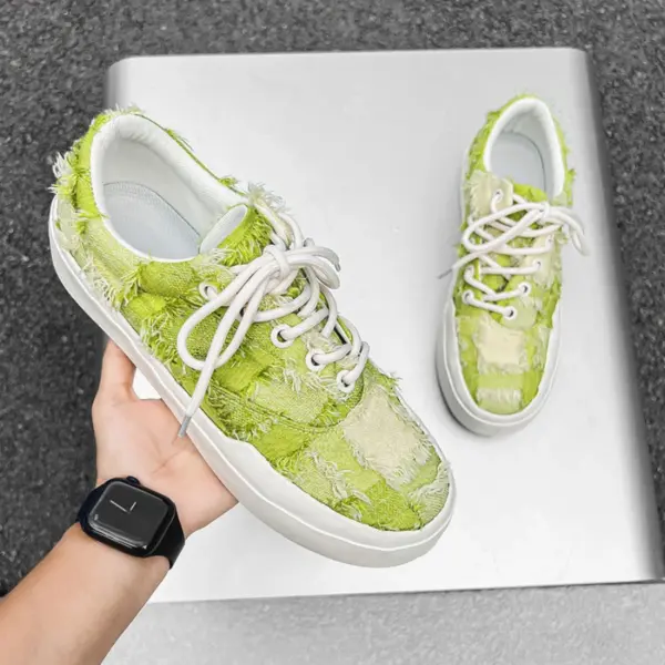 A hand holds Bulk Zapatos De Hombre custom classic embroidery skateboarding canvas shoes with green patchwork, frayed fabric, and white laces, displayed on a metallic surface—showcasing wholesale torn custom logo OEM ODM craftsmanship.