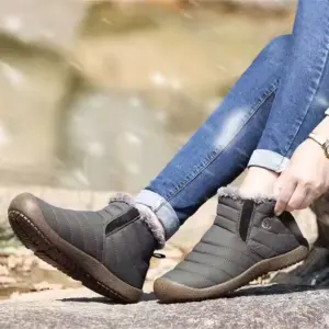 A person in blue jeans sits on a rock outdoors, adjusting one Factory Wholesale OEM ODM Low Top Waterproof Outdoor Cotton Snow Boot with fur lining.