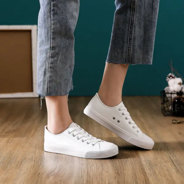 A person in frayed-hem blue jeans and Hot Sale Customize Fashionable PU Upper Women's Canvas Shoes stands on a wooden floor with decor in the background.