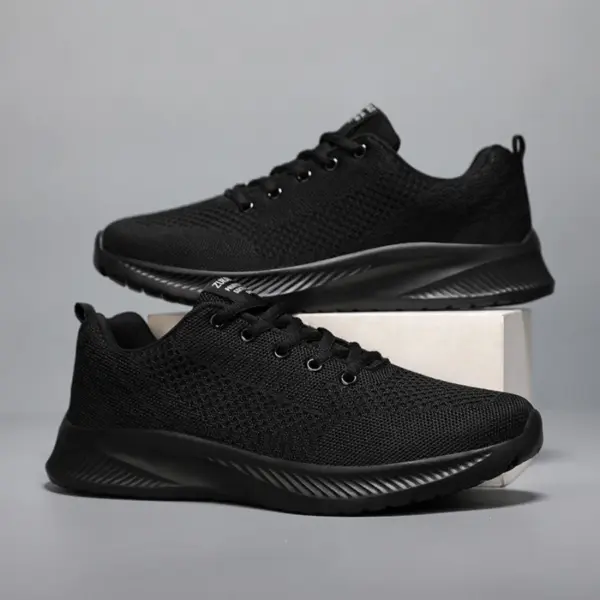A pair of Men's Casual Sneakers featuring black flying weaving mesh uppers and lightweight EVA soles, displayed on a plain gray background with one shoe resting on a white block.