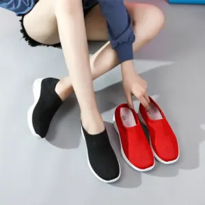 A person wearing black slip-on shoes sits on the floor and holds a pair of red High Quality Brand New Loafers Casual Knitted Mesh Running Custom Womens Tennis Shoes next to them.