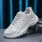 The OEM Trendy Tire Sole Men’s Light Anti-slip Wear Resistant Sneaker, featuring cotton mesh and EVA, is displayed atop a textured silver case against a blue curtain backdrop, highlighting its sporty chunky sole design for ODM or OEM orders.