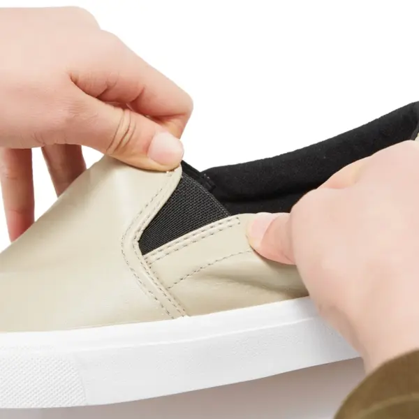 Close-up of hands stretching the elastic band of the Fashionable Casual Waterproof PU Upper Slip-on Flats Walking Shoes for Women in beige with a white sole.