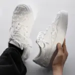 A person holds a pair of Bulk Zapatos De Hombre canvas shoes for men with classic embroidery and distressed fabric, viewed from above against a neutral background.