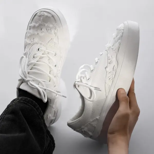 A person holds a pair of Bulk Zapatos De Hombre canvas shoes for men with classic embroidery and distressed fabric, viewed from above against a neutral background.