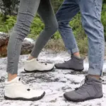 Two people in Factory Wholesale Direct Sale Fashion Outdoor Men Women Snow Boots and jeans stand face-to-face on a snow-dusted surface, with lush greenery in the background.
