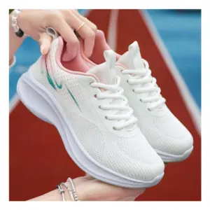 A person holds up 2024 Custom Mesh Sneakers Sport Women Running Shoes, white with pink and teal accents, set against a blurred red and blue track background.