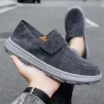 A person holds a New Retro Men Shoes Light Shock Absorbing Flat Sneaker, a customizable leather loafer with a thick rubber sole, displaying this OEM ODM footwear outdoors on an asphalt surface.