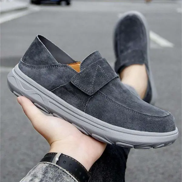 A person holds a New Retro Men Shoes Light Shock Absorbing Flat Sneaker, a customizable leather loafer with a thick rubber sole, displaying this OEM ODM footwear outdoors on an asphalt surface.