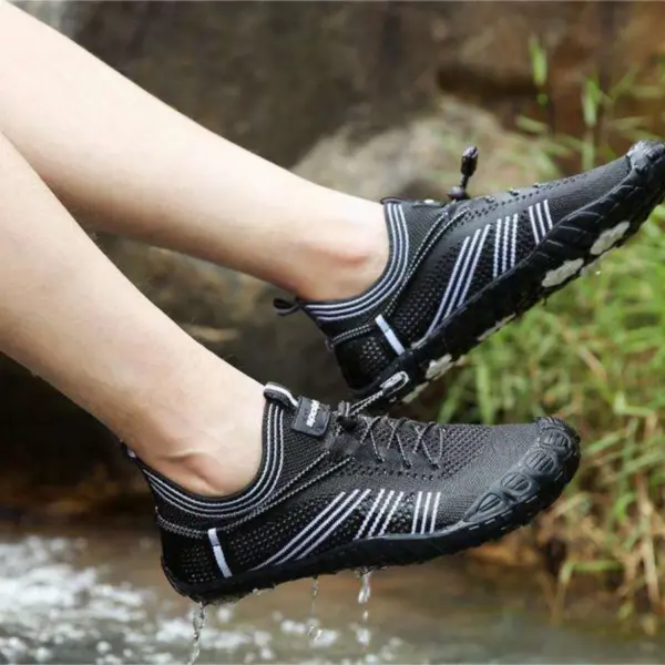 A pair of feet wearing black Customized Anti-slip Quick Drying Outdoor Shoes Flat Mesh Sports Flats Laced Beach Water Shoes with white stripes are held above the ground, water dripping from the soles.