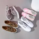 Four pairs of Hot Sale Casual Low Top No Lace Lazy Canvas Shoes for Women, customizable via OEM/ODM, are arranged on a gray surface: pink leopard, tie-dye pink, brown leopard, and plain white with random fluff decoration.
