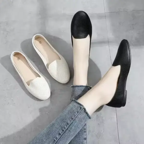 A person wearing black Flat Shoes Ballet Flat for Ladies Office sits on a grey floor, with a similar white pair placed nearby.