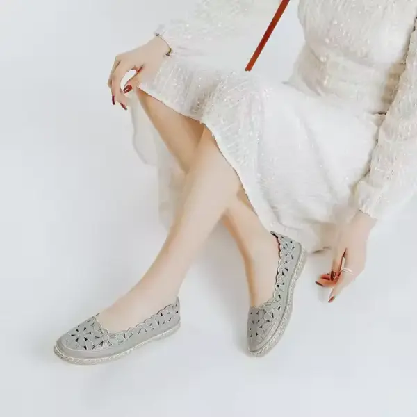 A woman in a white long-sleeve dress sits with legs crossed, wearing Office Round Toe Dress Flat Shoes in light grey that feature stylish cut-out patterns.
