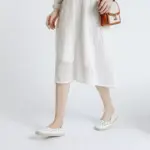 A person in a textured white dress and Office Round Toe Dress Flat Shoes holds a small brown handbag, standing against a plain white background—ideal for OEM ODM fashion showcases.