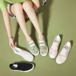 A person on a green floor tries on XRH Wholesale Pink Slip-on Women's Casual Canvas Shoes, with OEM ODM options—two other pairs in unique patterns and one solid black pair beside them.