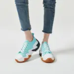 A person wearing light blue XRH Wholesale Plain Casual Custom Logo Mujer Ladies Sneakers with white laces and chunky black-brown wave-patterned soles, paired with cropped blue jeans, stands on a white background.