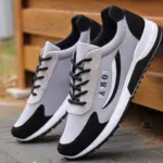 A pair of High Quality Gym Casual Cushioning Sneakers for men in gray and black, with "FASHION" on the side, displayed outdoors near a wooden structure.