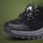 Close-up of a Wholesale Black Mixed Anti-slip Women Snow Boot, featuring TPR, PU, canvas, plush lining, and laced cotton design with water droplets on its surface against a green background.
