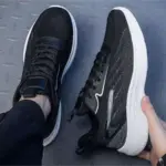 A person wearing one Custom Wholesale Men Shoes Shock Rebound OEM Outdoor Running Sneaker holds the other above a textured gray surface.