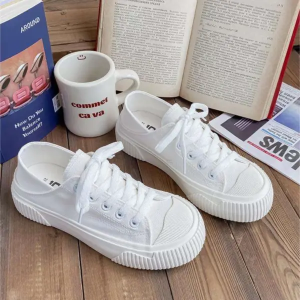 A pair of Breathable Designed Women Shoes Solid Cotton Sneakers Slip on Low Top Women Canvas Shoes sits on a wooden surface beside an open book, a mug, a magazine, and a box featuring images of nail polish bottles.