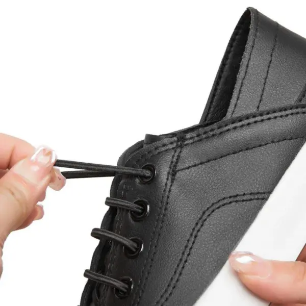 A person is threading a black elastic OEM ODM shoelace through the eyelets of Fashion Low Top PU Upper Casual Shoes—black flat walking canvas sneakers for women with white soles.