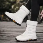 A person wearing 2025 Spring Wenzhou Factory Zipper Women Casual Waterproof Fur Winter Outdoor Medium Snow Boots, featuring stylish fur trim and black soles, sits outdoors in black leggings—perfect for showcasing chic footwear.
