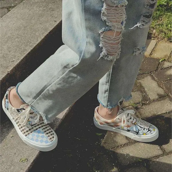 A person in ripped light blue jeans and Wholesale Mixed Wearable Canvas Shoes Lace up Breathable Sneakers Low Top Rubber slip on Loafers stands on a paved walkway and grass.