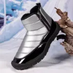 The New Down Fabric Waterproof Snow Boots for men, featuring double zippers, a ridged sole, and thickened cotton lining, are available for OEM ODM orders and displayed propped against wood in a snowy setting.
