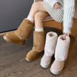 A woman in a light sweater and skirt tries on tan fur boots while holding white ones, sitting on a wooden floor—ideal for showcasing Wholesale Winter Plus Plush Platform Non-slip Snow Boots Cotton Floette Plush Shoes for Ladies in OEM ODM footwear collections.