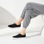 Woman seated on a white chair in a minimalist indoor setting, wearing gray joggers and Hot Sale Casual Low Top No Lace Lazy Canvas Shoes Slip on Random Fluff Decoration for Women—great inspiration for OEM ODM fashion.