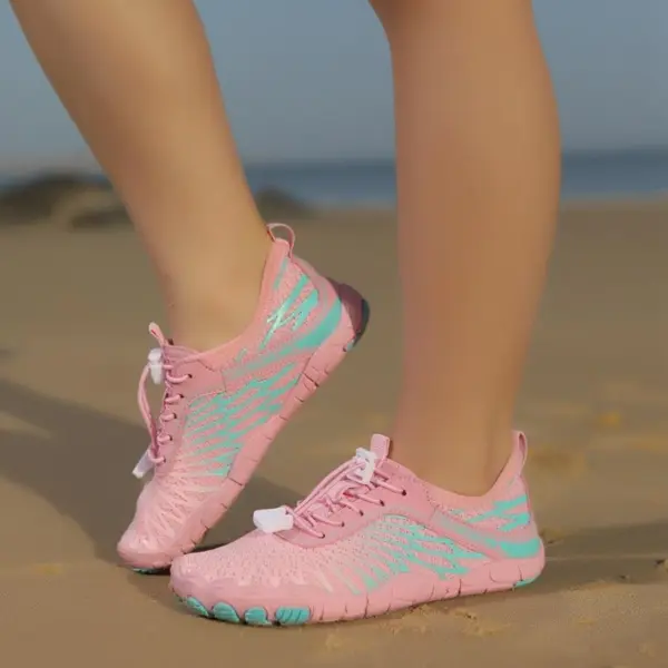 A person stands on sandy ground, one foot slightly raised, wearing Wholesale Customized Outdoor Beach Flat Anti-slip Breathable Sneakers Swimming Sports Children Shoes in pink and turquoise.