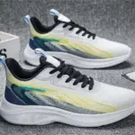 A pair of Custom Wholesale Men Shoes Shock Rebound OEM Outdoor Running Sneakers in white with black laces and blue-yellow gradient accents rests on a gray textured surface—ideal for light, breathable, customizable athletic wear.