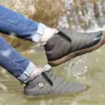 Wearing gray Factory Wholesale OEM ODM low top waterproof outdoor cotton snow boots, a person in rolled-up blue jeans splashes water in a shallow stream.