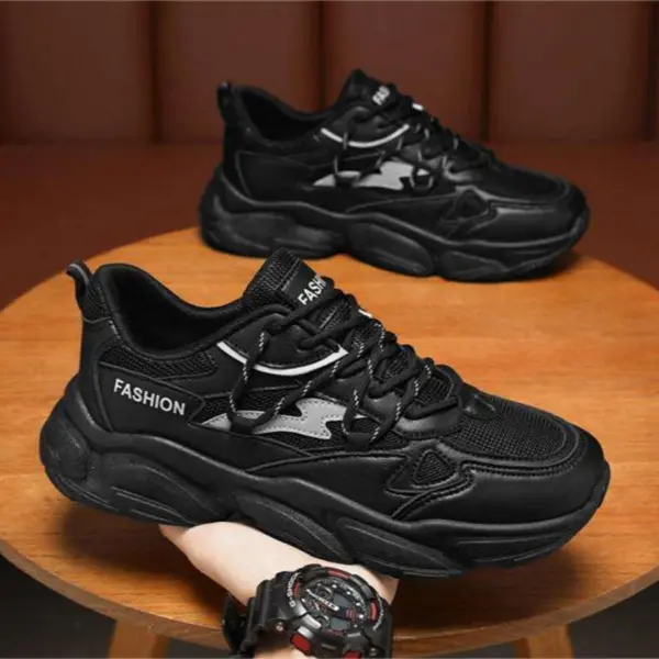 A hand holds a black Wholesale Factory Customized Solid Color Daily Sports Outdoor Shoe made of PU mesh, while an identical men's walking sneaker rests on a wooden surface in the background.