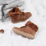 The 2025 Colorful Boots Women Shoes, featuring plush faux suede and warm lining, are stylish outdoor ankle boots for ladies, ideal for OEM/ODM orders. They are shown on snow near a gray stone and a pine cone.