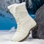 The OEM ODM 2025 large size round toe snow boots, made of PU and TPR with a warm cotton lining, are shown propped against a rock in the snow, trees in the background. Suitable for men and women, perfect for daily winter wear.