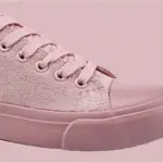 A close-up of Wholesale Factory Painted Plush Solid Canvas Shoes—adult sports flat sneakers with pink textured fabric, laces, and a rubber toe cap and sole—set against a matching pink background.
