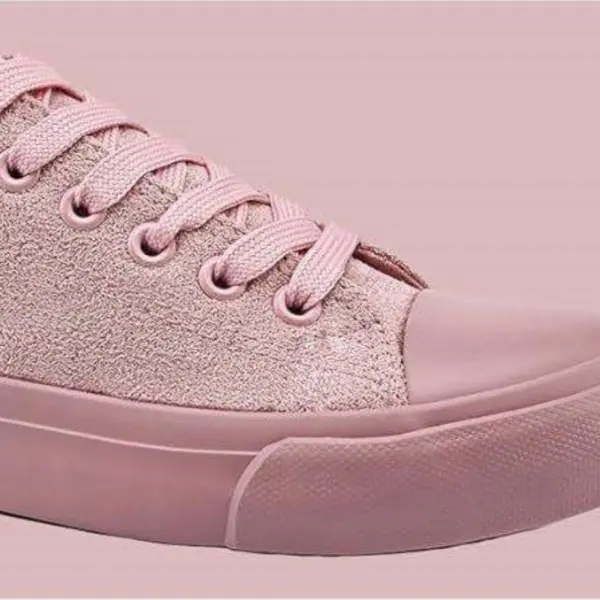 A close-up of Wholesale Factory Painted Plush Solid Canvas Shoes—adult sports flat sneakers with pink textured fabric, laces, and a rubber toe cap and sole—set against a matching pink background.